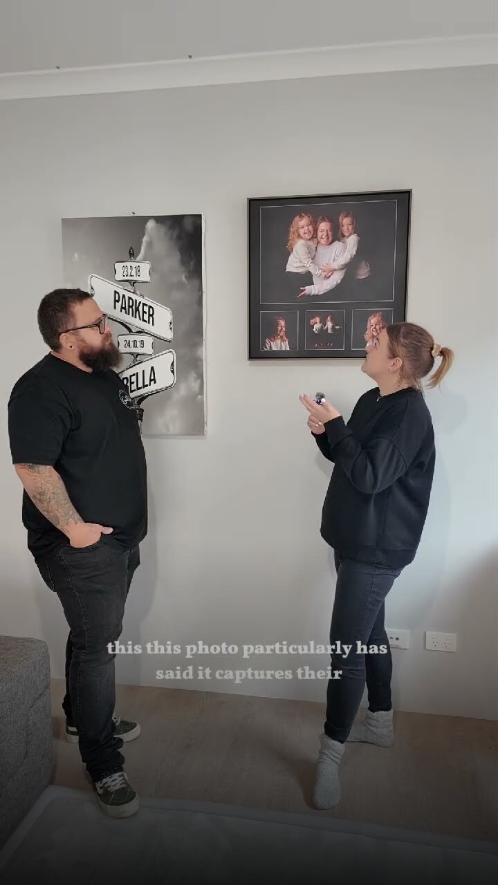 A Good Life Portraits couple at home, looking up at their framed family portrait and canvas on the living room wall