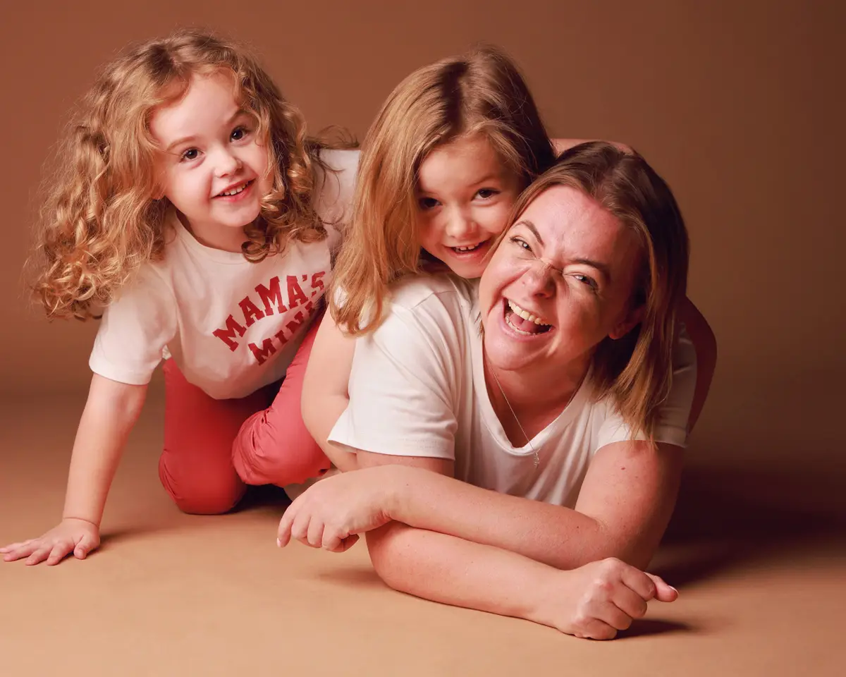 A mother lying on the studio floor laughing with her two young daughters