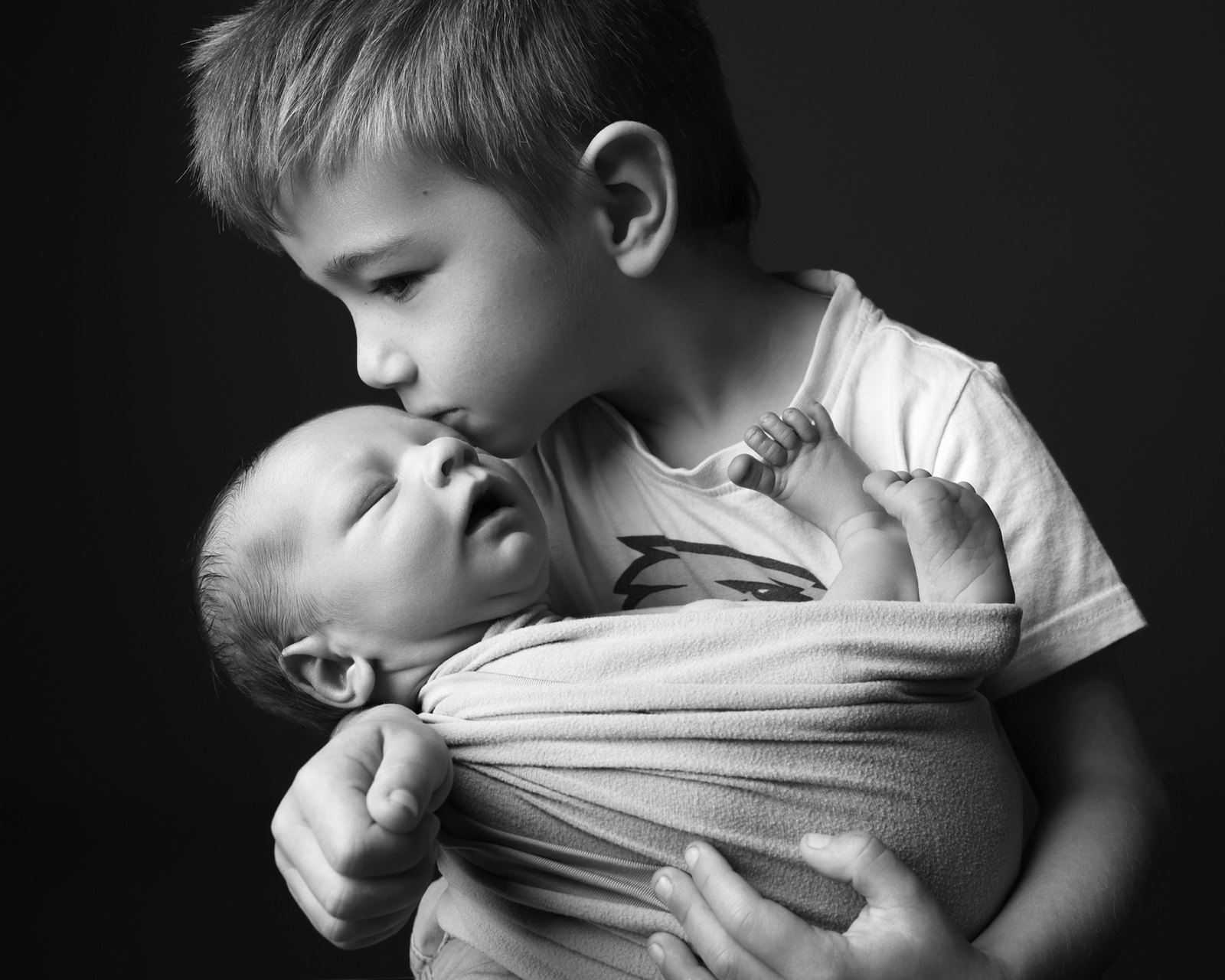 A big brother holding his newborn sibling, in black and white