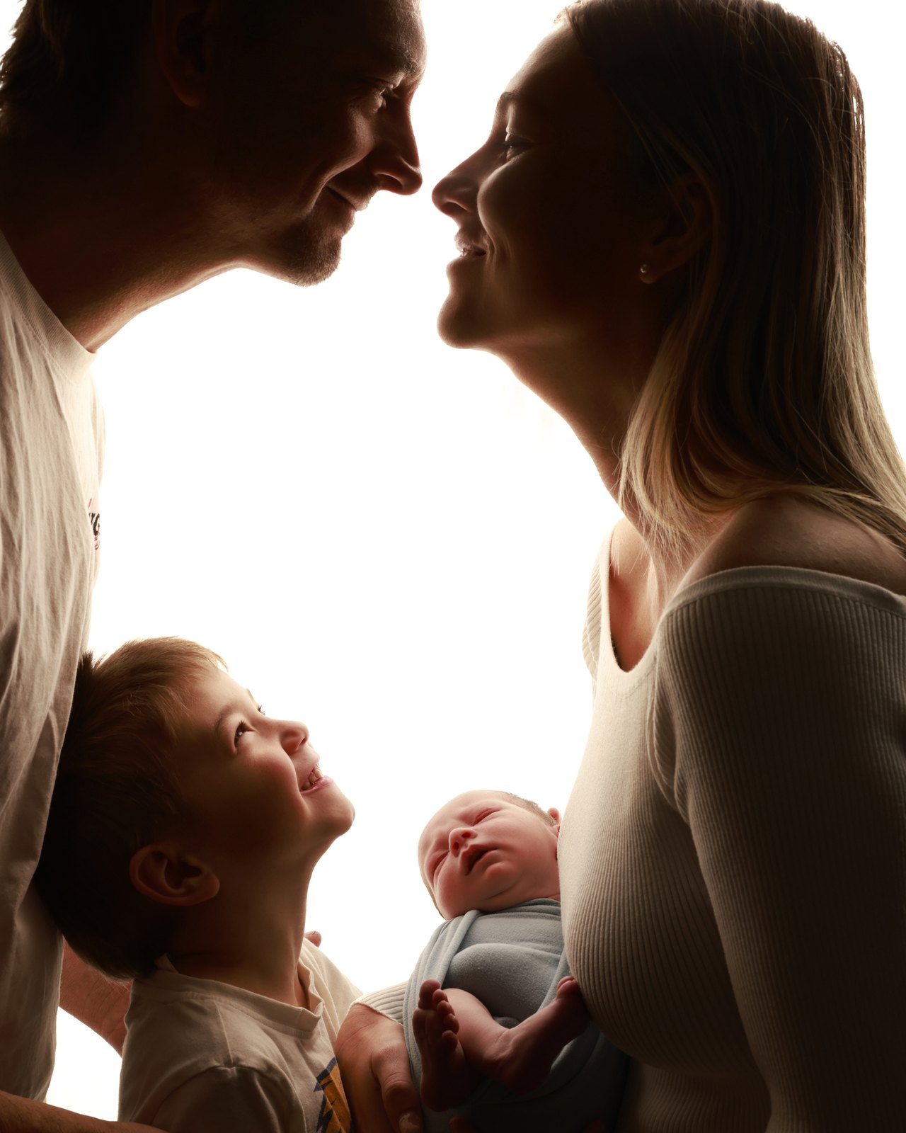 New parents holding their newborn baby between them, backlit in the studio